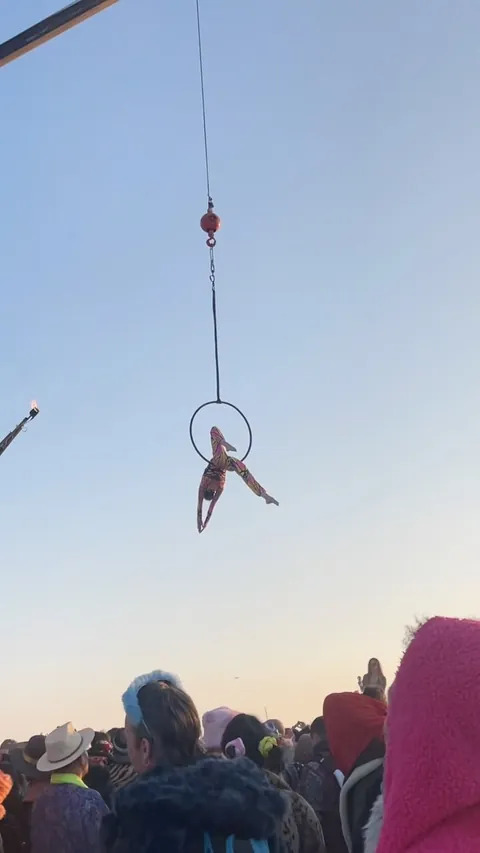 Aerial hoop suspended from a crane at sunset over the Burning Man crowd