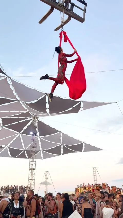 Red aerial hammock rigged from a shade structure at Burning Man